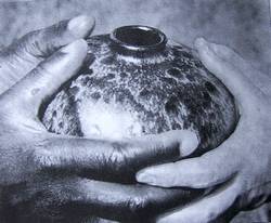 Zwei Hände halten vorsichtig einen texturierten, runden Keramiktopf.