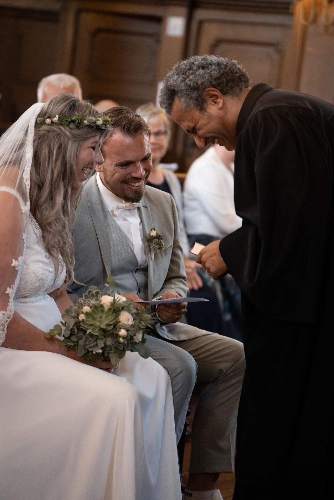 Pfarrer David Gabra beugt sich zu einem Brautpaar herunter, beide lächeln