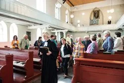 Menschen verlassen die Hoffnungskirche nach einem Gottesdienst, angeführt von einer Frau in Amtstracht.