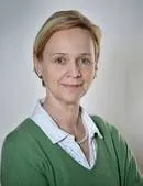 Porträt einer lächelnden Frau mit kurzen blonden Haaren und grünem Pullover.