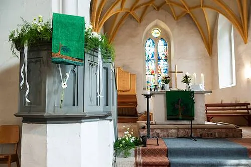  Geschmückter Kircheninnenraum mit Kanzel, Altar, Buntglasfenster und Gewölbedecke.